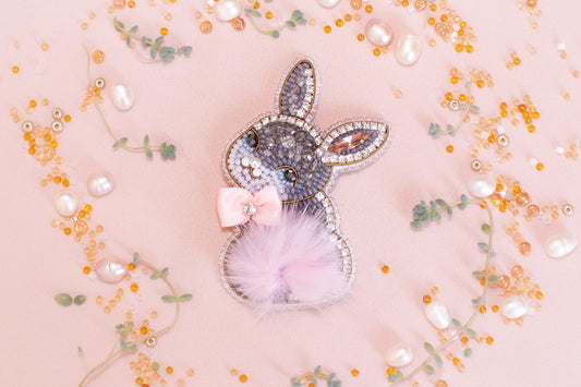 a decorative Easter bunny charm adorned with rhinestones and pearls, surrounded by scattered beads and sequins in shades of pink and gold.