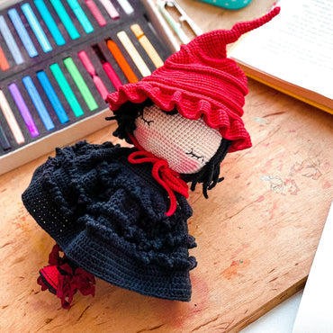 a crocheted doll with a red hat on a wooden table