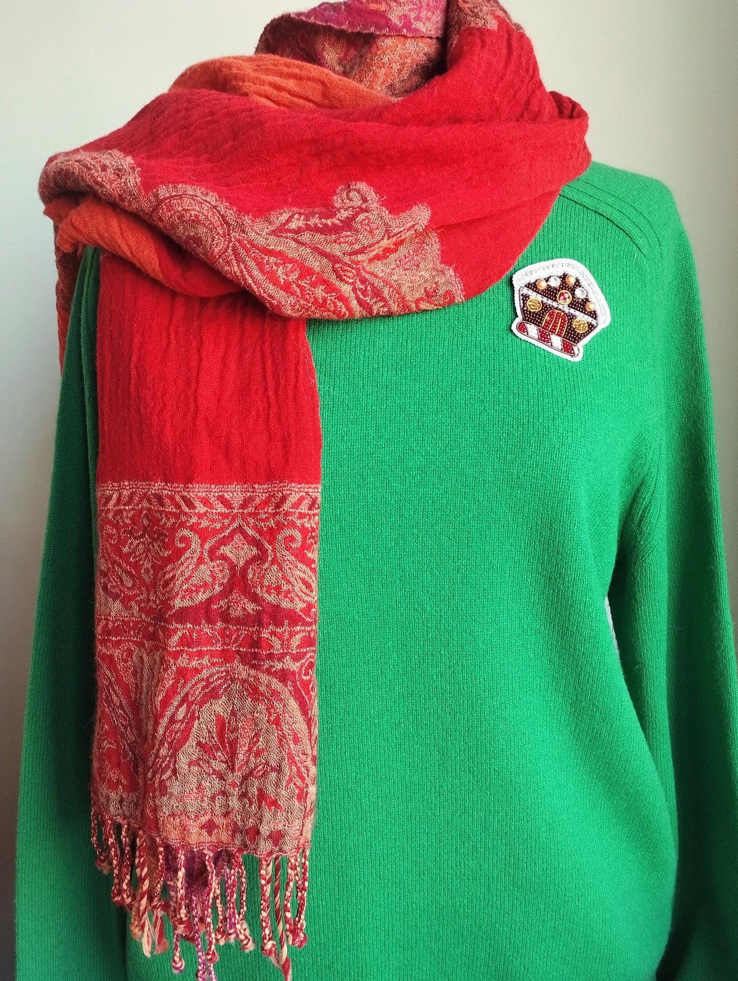 A person wearing a green sweater and a red and orange patterned scarf.