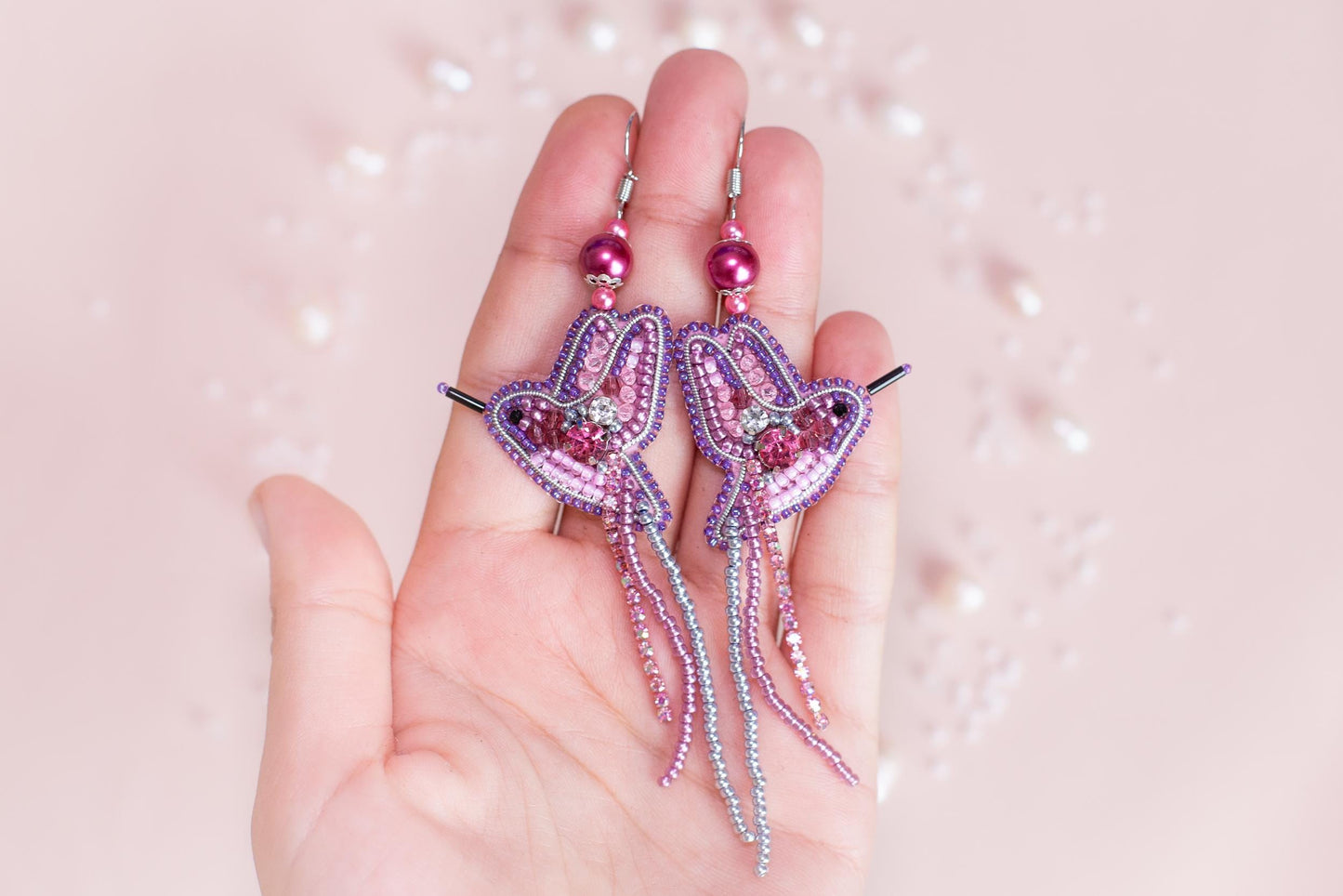 a hand holding a pair of pink beaded earrings