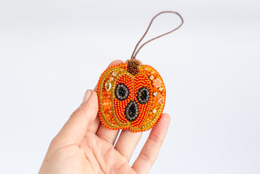 a hand holding a beaded pumpkin ornament