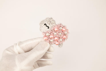 a white glove holding a pink beaded brooch