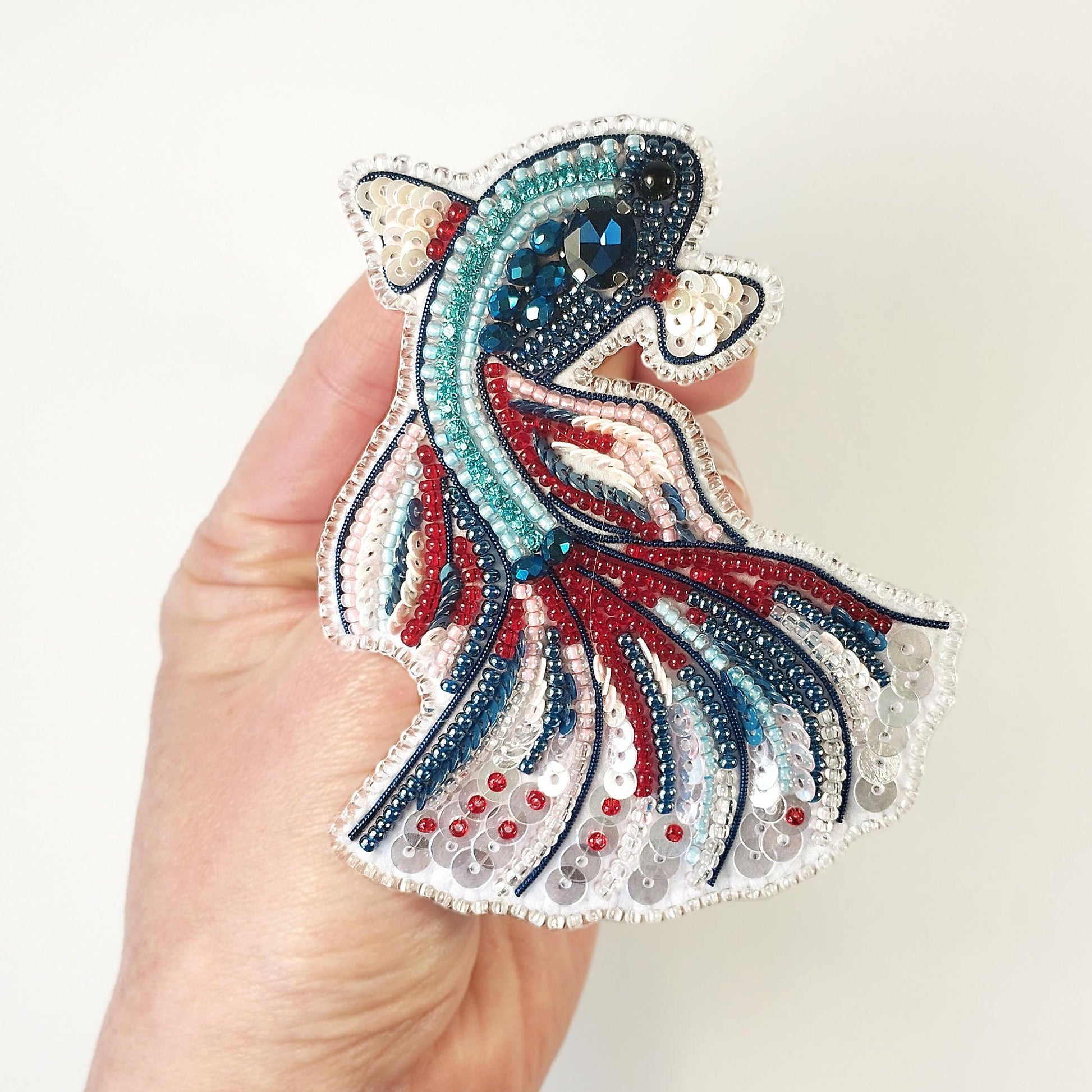 a hand is holding a colorful fish brooch