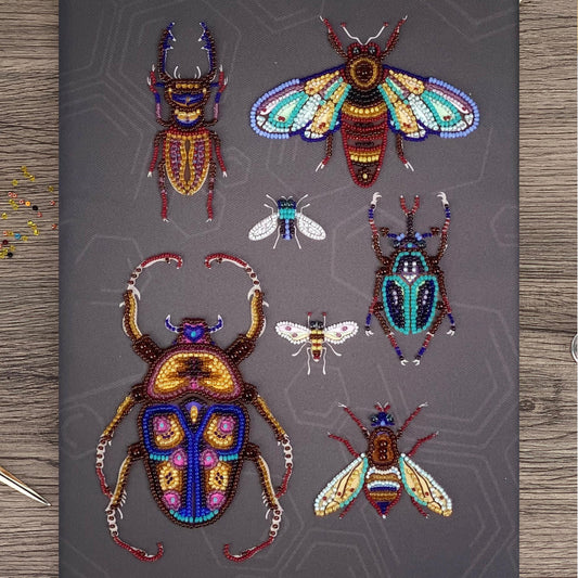 a collection of six intricately designed, colorful, and detailed insects, including a large dragonfly, a bee, a butterfly, a ladybug, a praying mantis, and a grasshopper, all crafted from beads.