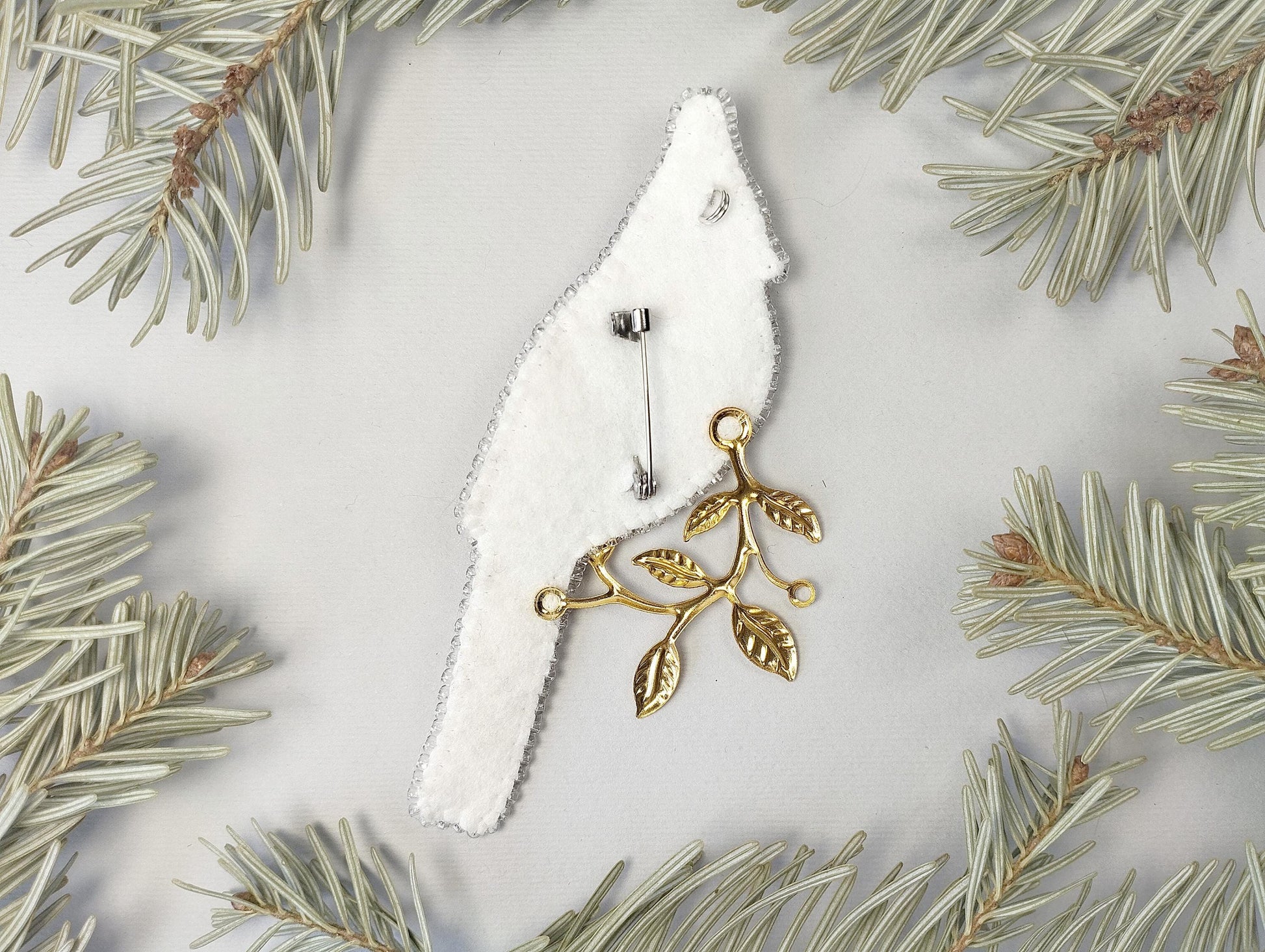a white and gold bird ornament hanging from a pine tree