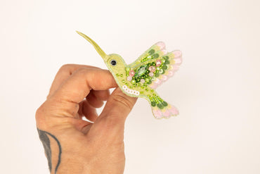 a hand holding a small green and pink bird