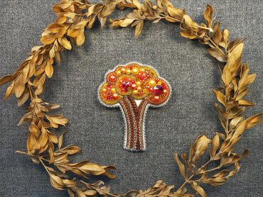 a brooch with a tree on it surrounded by leaves