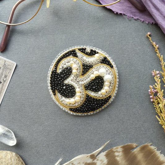 a circular, ornate piece of jewelry with a black and gold design, surrounded by various objects such as a pair of glasses, feathers, and crystals.