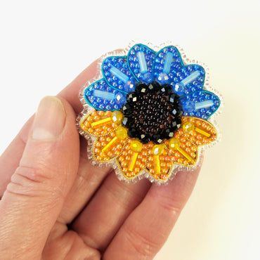a hand holding a blue and yellow flower brooch