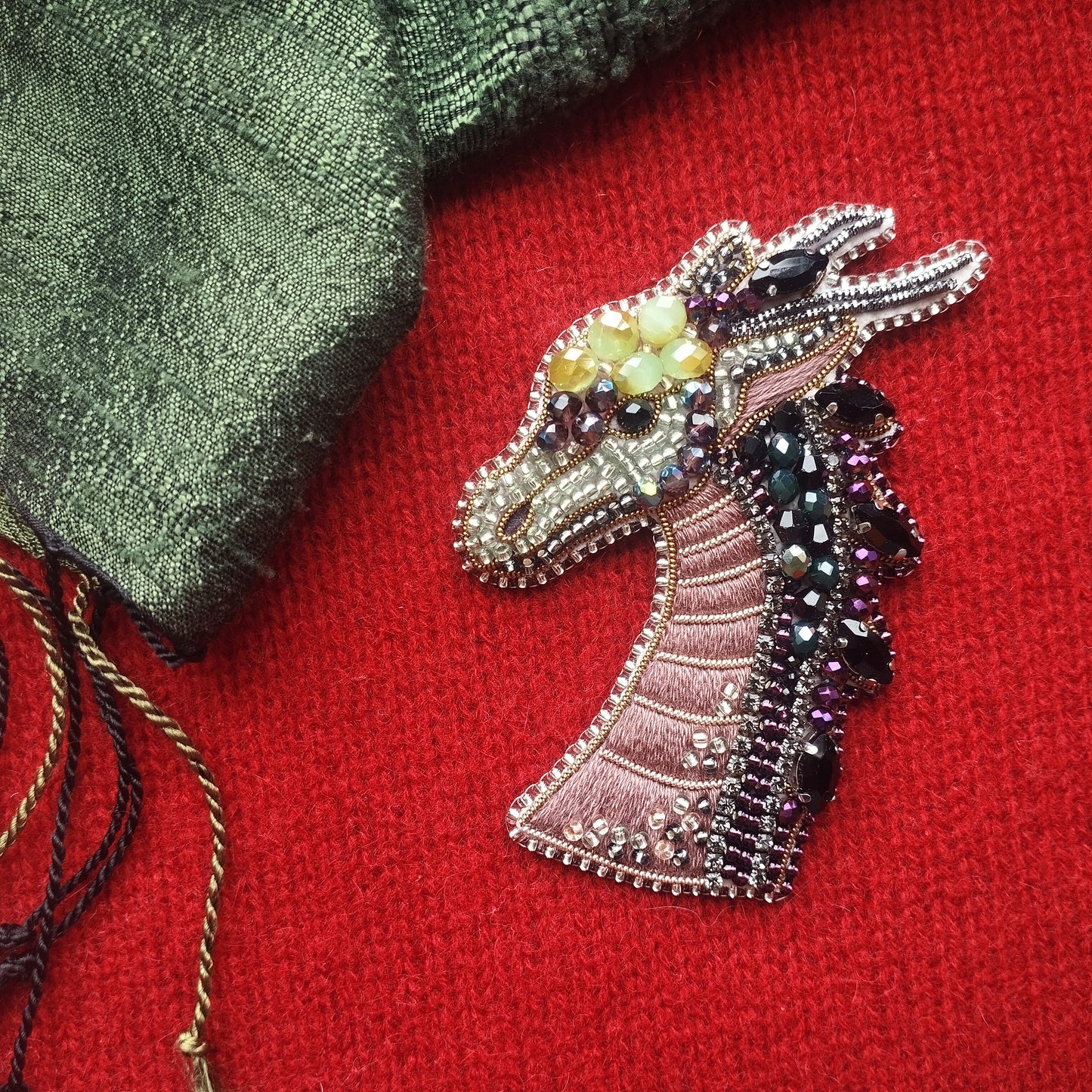 a close-up of a decorative dragon brooch with intricate beading and embellishments, placed on a red fabric surface.