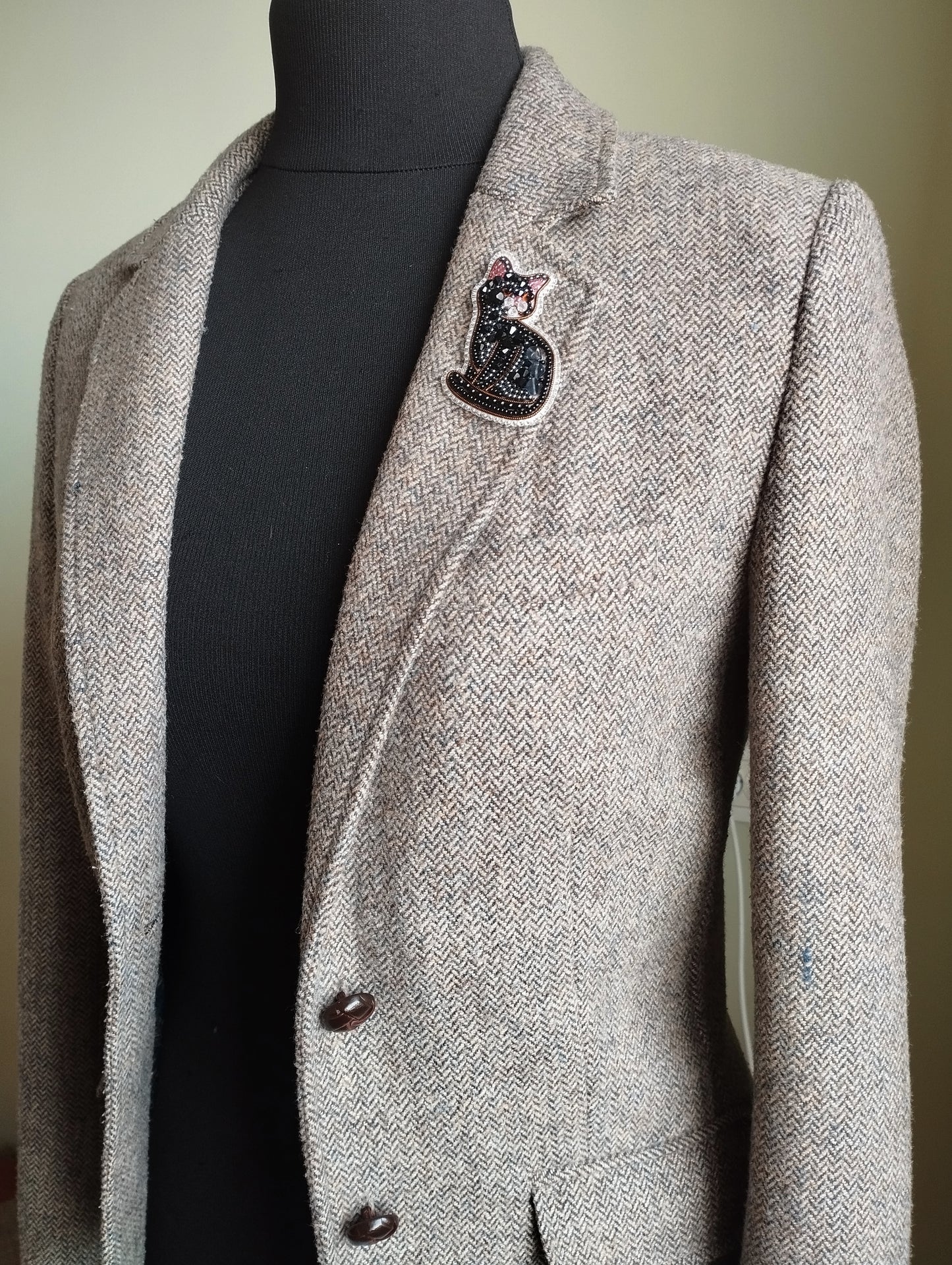 A gray tweed blazer with a black cat brooch on the left breast pocket area.