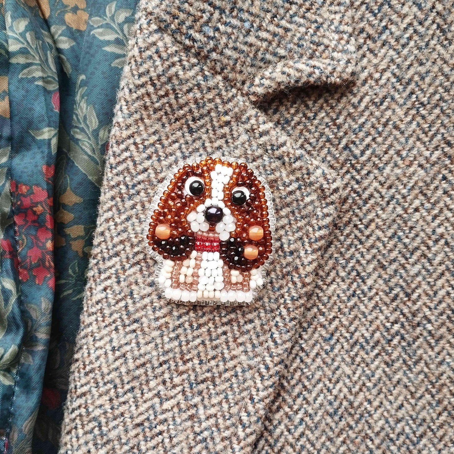 A close-up of a beaded embroidered dog pin on a tweed jacket.