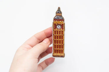 a person is holding a brooch with a clock on it