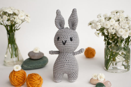 a crocheted bunny standing next to a vase of flowers