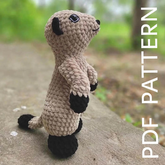 A crocheted toy meerkat with black and beige fur, standing on a concrete surface with a blurred natural background.