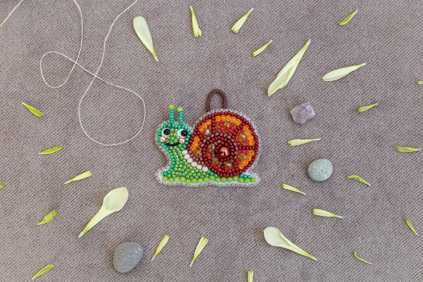 a colorful bead necklace with a snail design, surrounded by various natural elements such as leaves, stones, and a string.