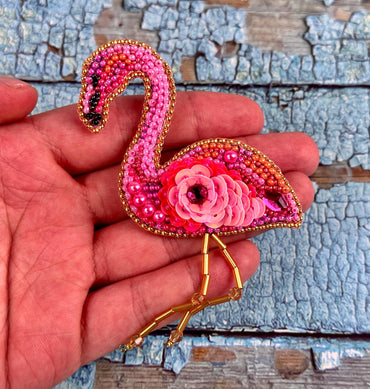 a hand holding a pink flamingo brooch