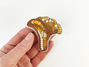 a hand holding a beaded brooch in the shape of an elephant