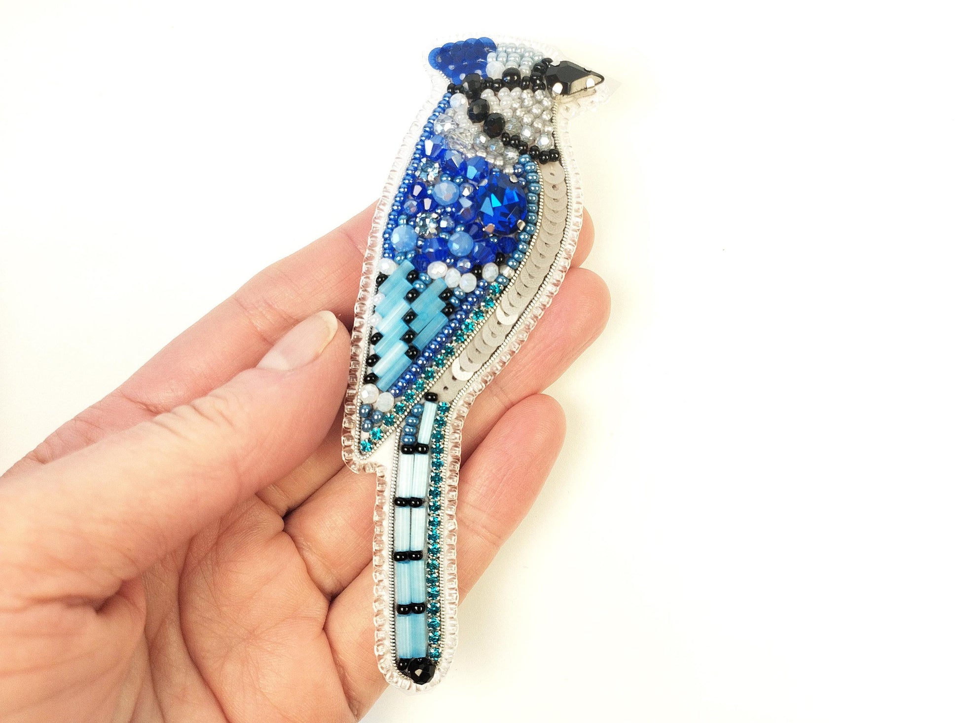 a hand holding a blue bird brooch in it's left hand