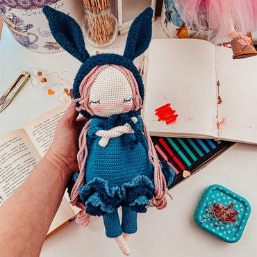 a crocheted doll in a blue dress next to an open book