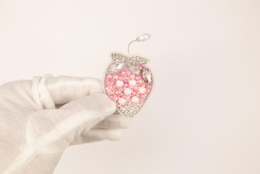 a hand in white gloves holding a pink heart ornament