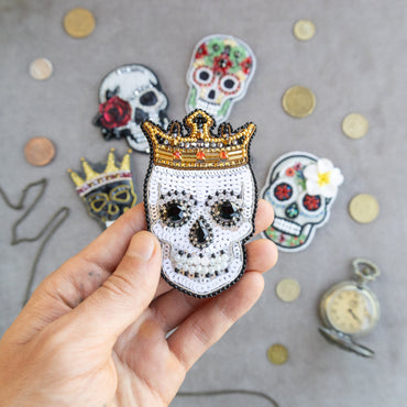 a hand holding a small skull with a crown on top of it