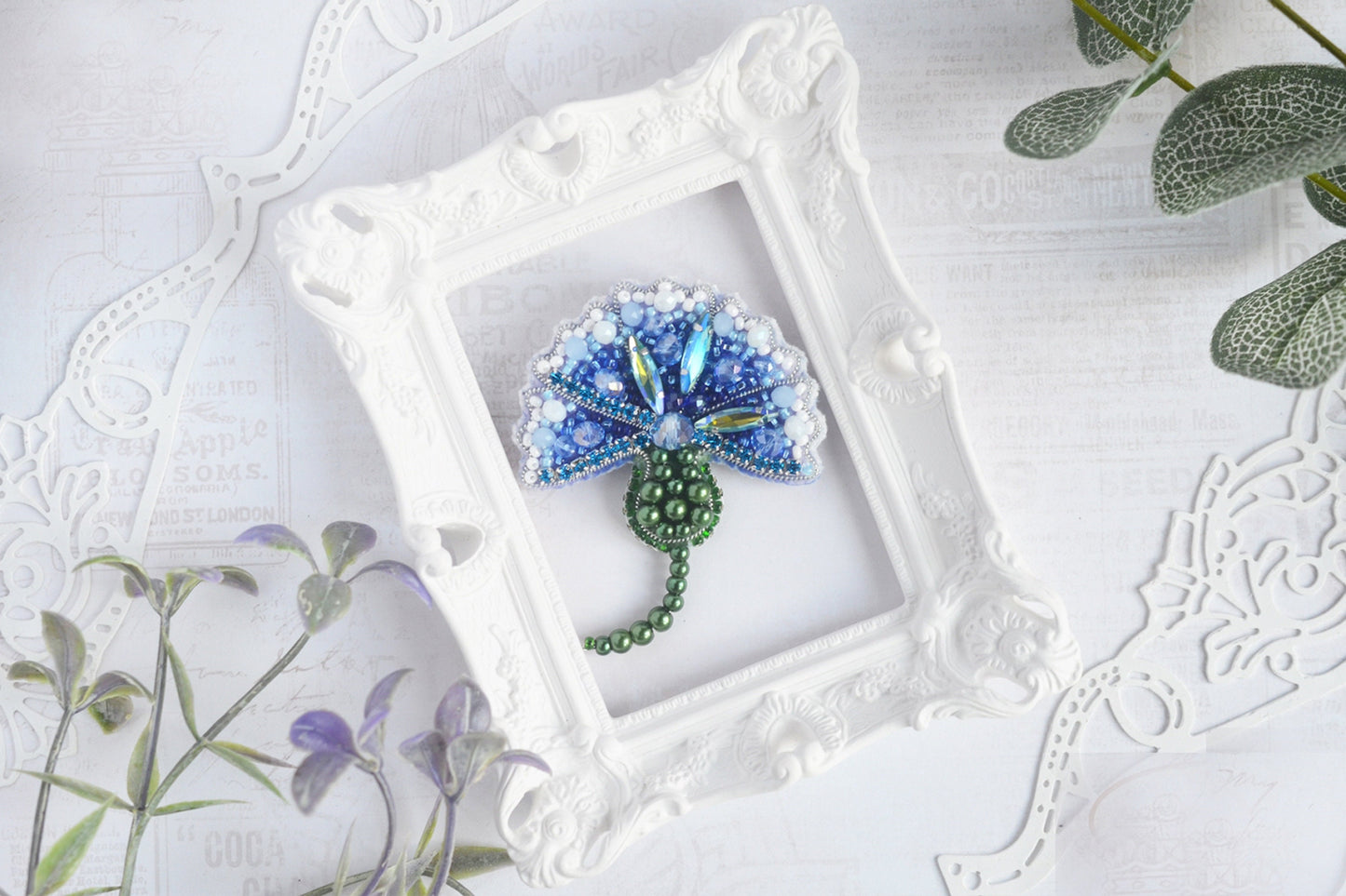 a blue and green brooch sitting in a white frame