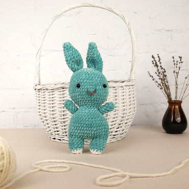 a crocheted blue bunny sitting next to a white basket