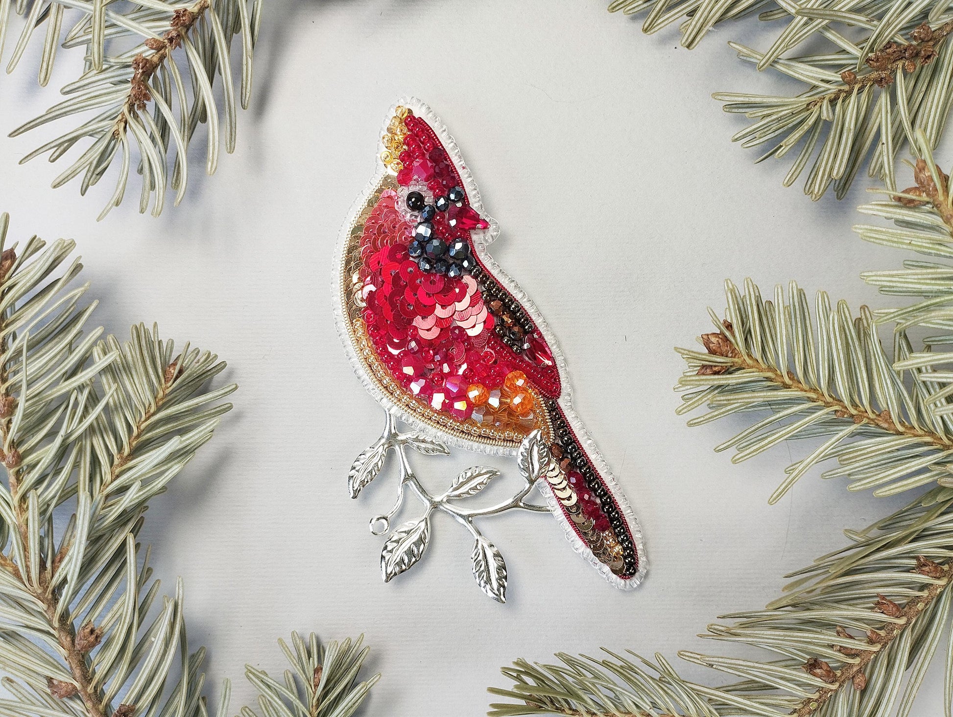 a red bird ornament hanging from a pine tree