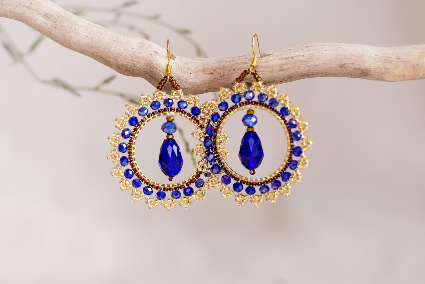 a pair of blue and gold earrings hanging from a branch