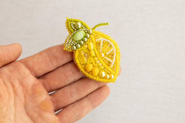 a hand holding a yellow beaded brooch
