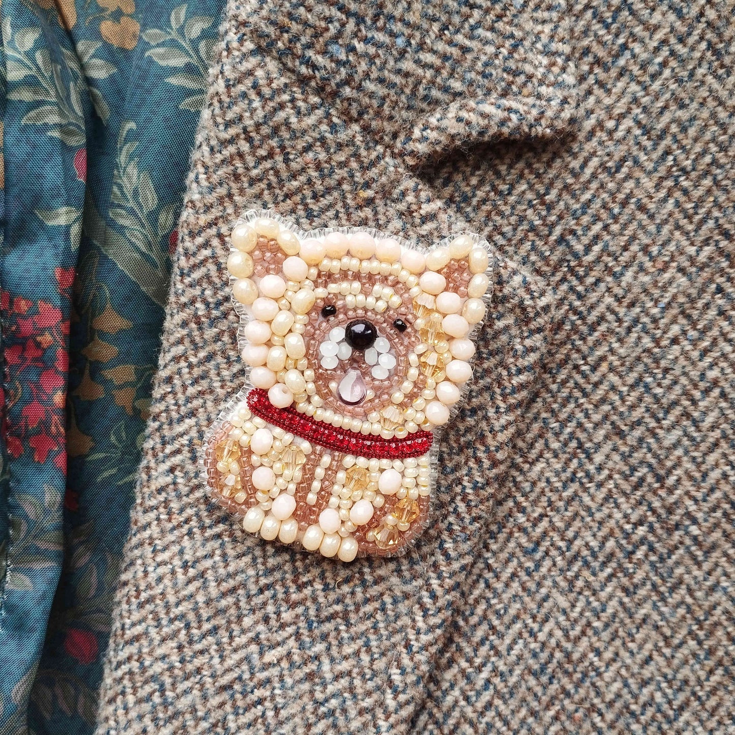 A close-up image of a beaded dog pin or brooch on a tweed jacket.