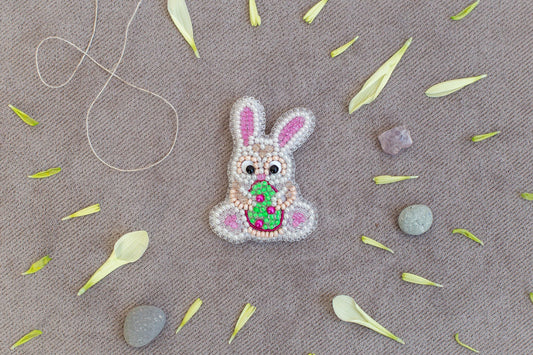 a small, intricately designed Easter bunny made of beads and flowers, surrounded by various natural elements such as leaves, stones, and a string.