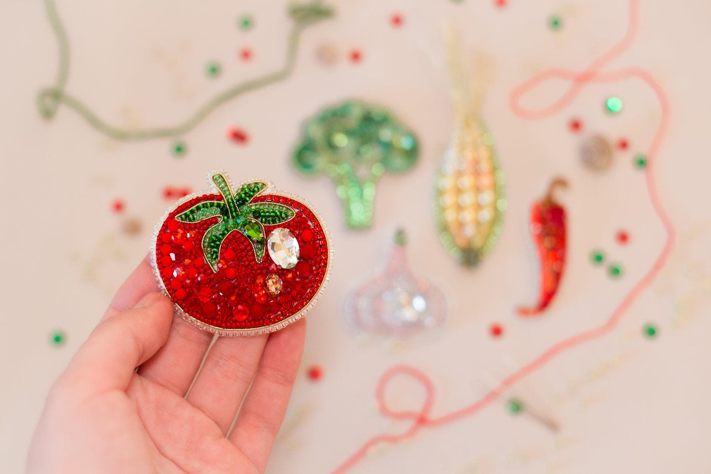 a hand holding a small red strawberry brooch