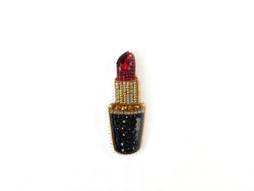 A decorative piece featuring a red lipstick with a gold and black design, including rhinestones and a gemstone.