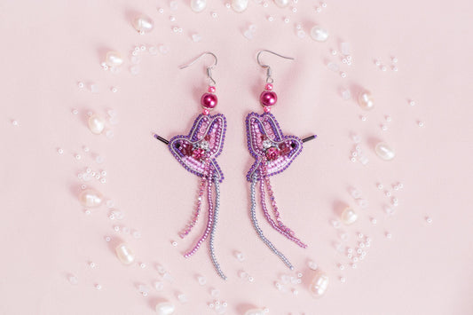 a pair of pink and purple earrings on a pink background
