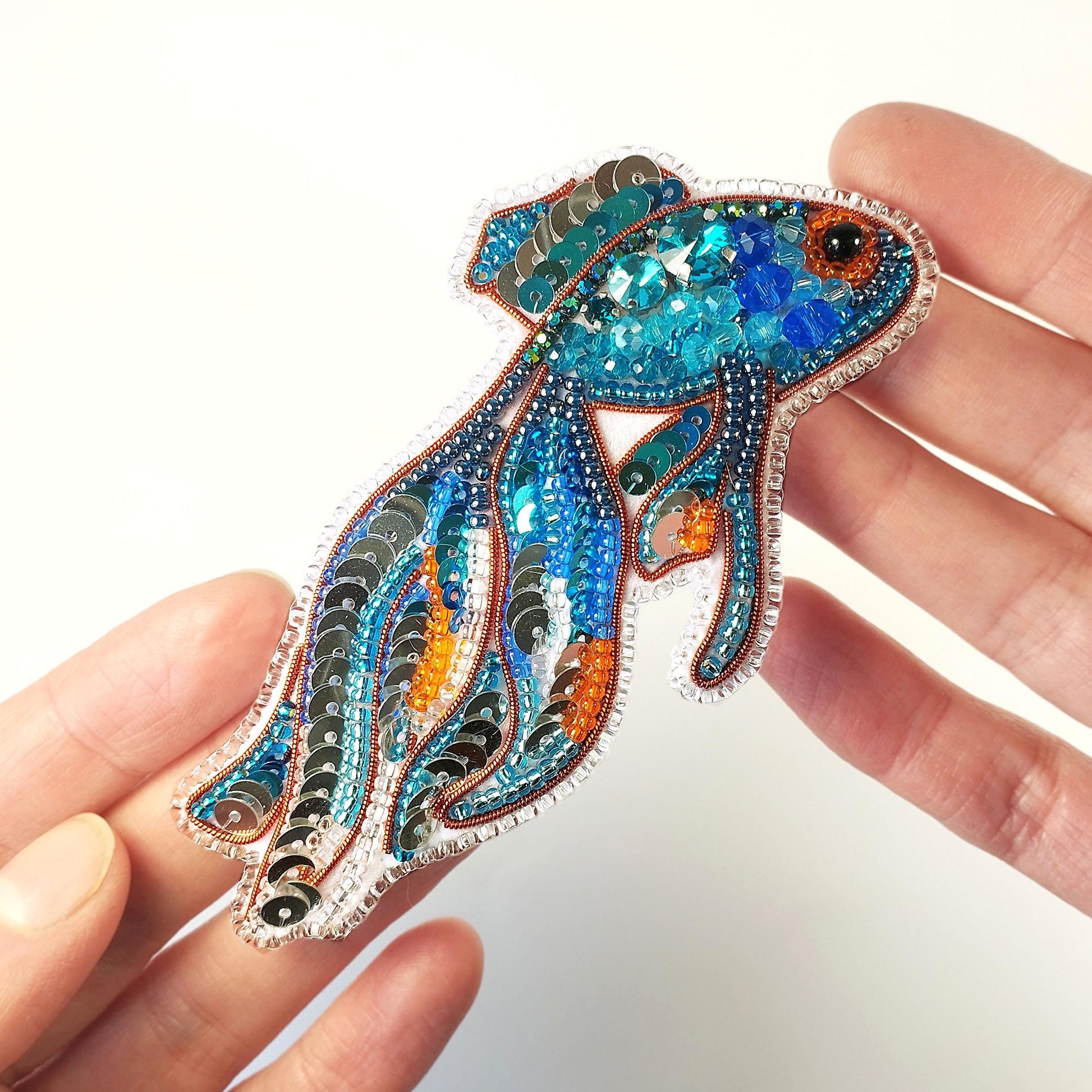 a hand holding a blue and orange fish brooch