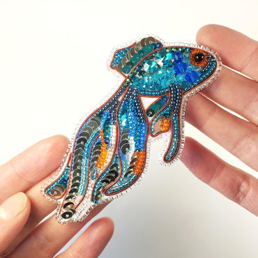 a hand holding a blue and orange fish brooch