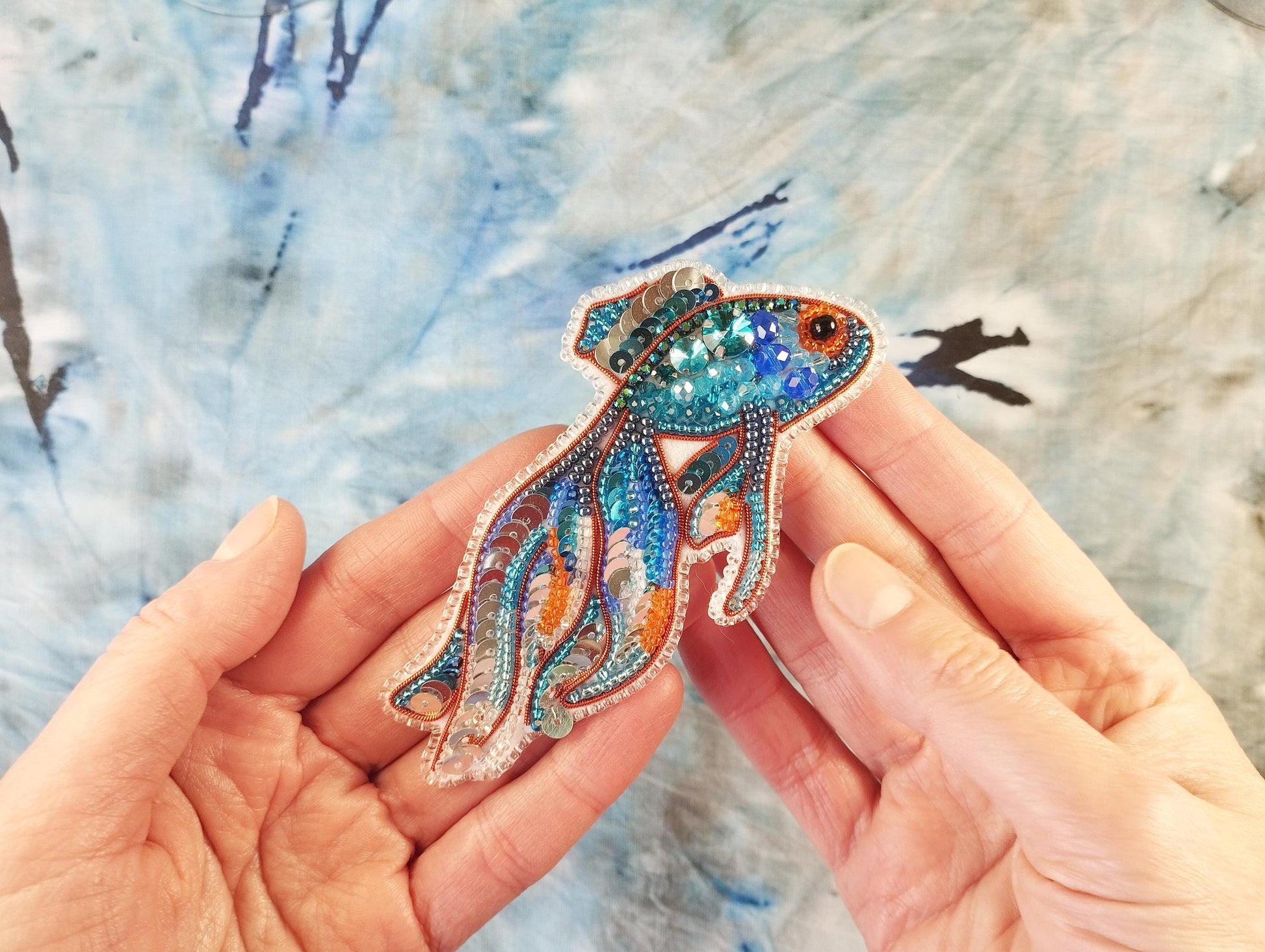 a person holding a brooch with a fish design on it