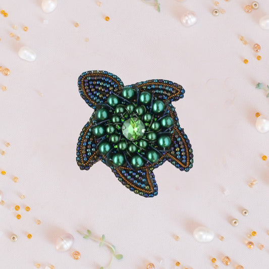 a green beaded brooch sitting on top of a table