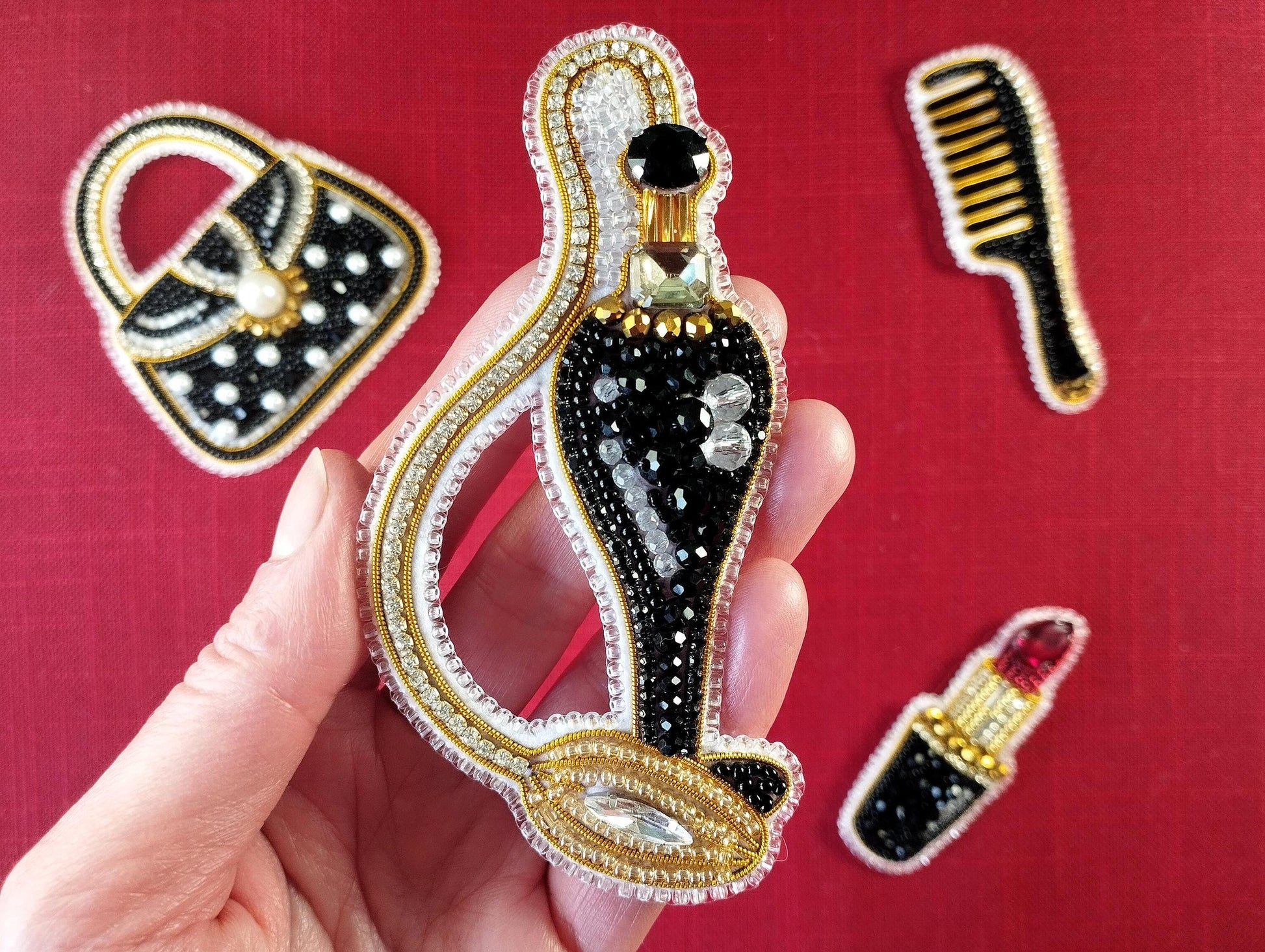 A hand holding a decorative piece of jewelry, which appears to be a brooch or pendant, against a red background.