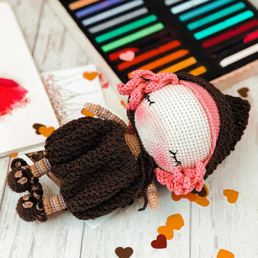 a crocheted doll laying on a table next to a crochet book