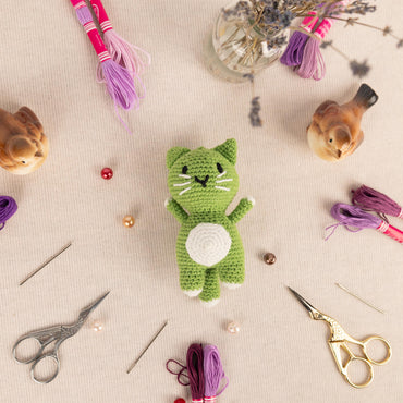 a green cat sitting on top of a table next to a pair of scissors