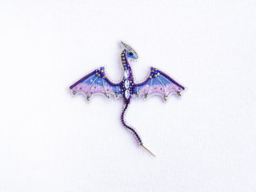 a purple and blue dragon brooch sitting on top of a white surface