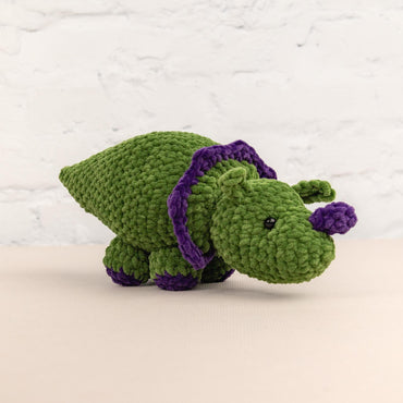 a crocheted green stuffed animal with a purple ribbon around its neck