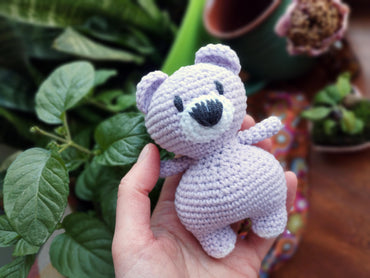a hand holding a small crocheted teddy bear