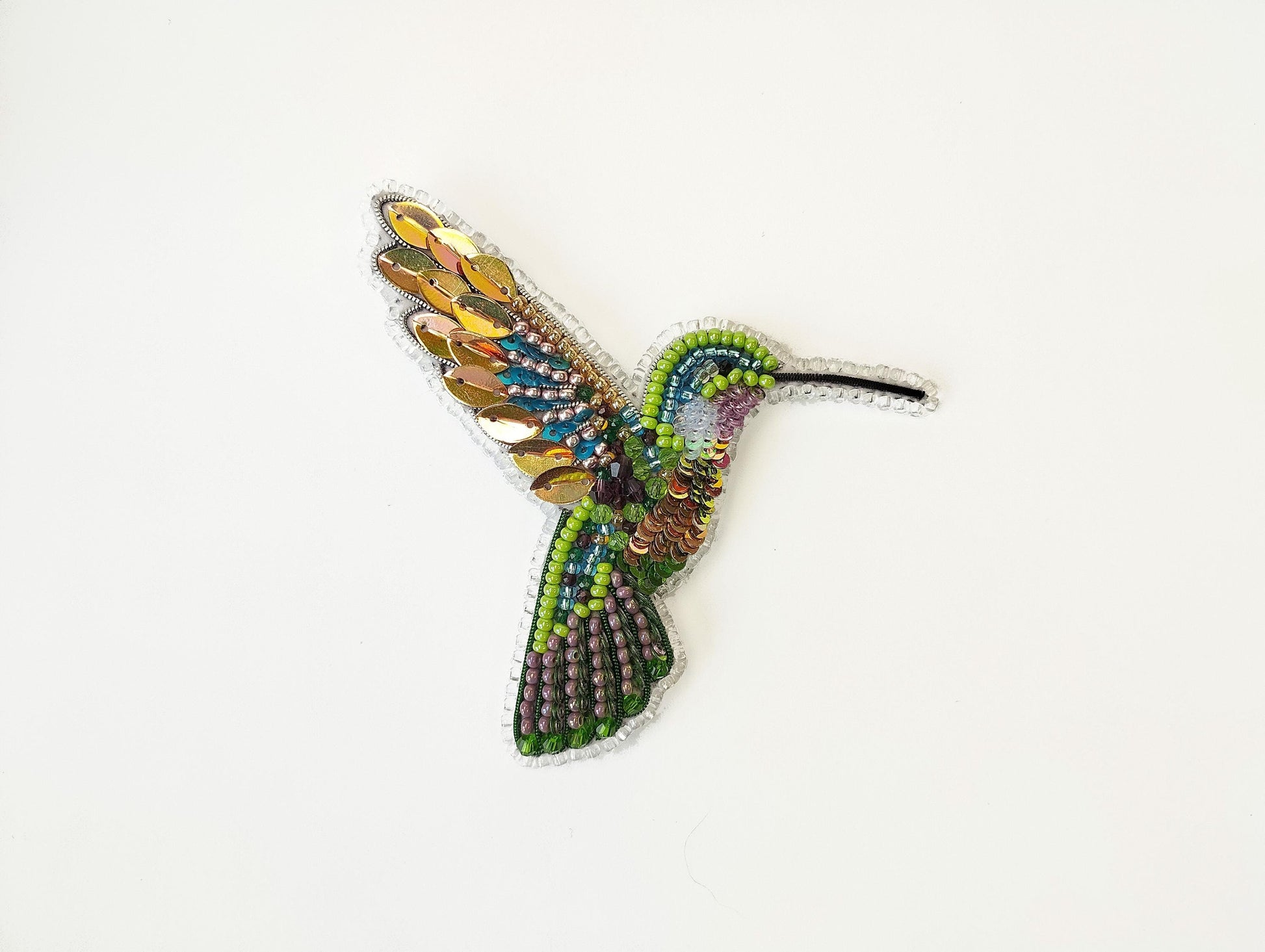 a beaded hummingbird brooch sitting on a white surface