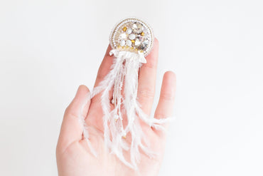 a woman's hand holding a brooch with feathers