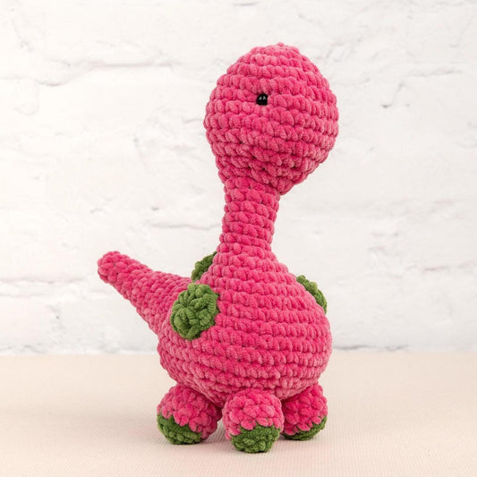 a crocheted pink dinosaur sitting on a table