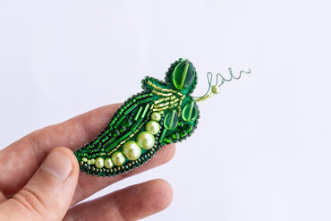 a hand holding a green beaded brooch